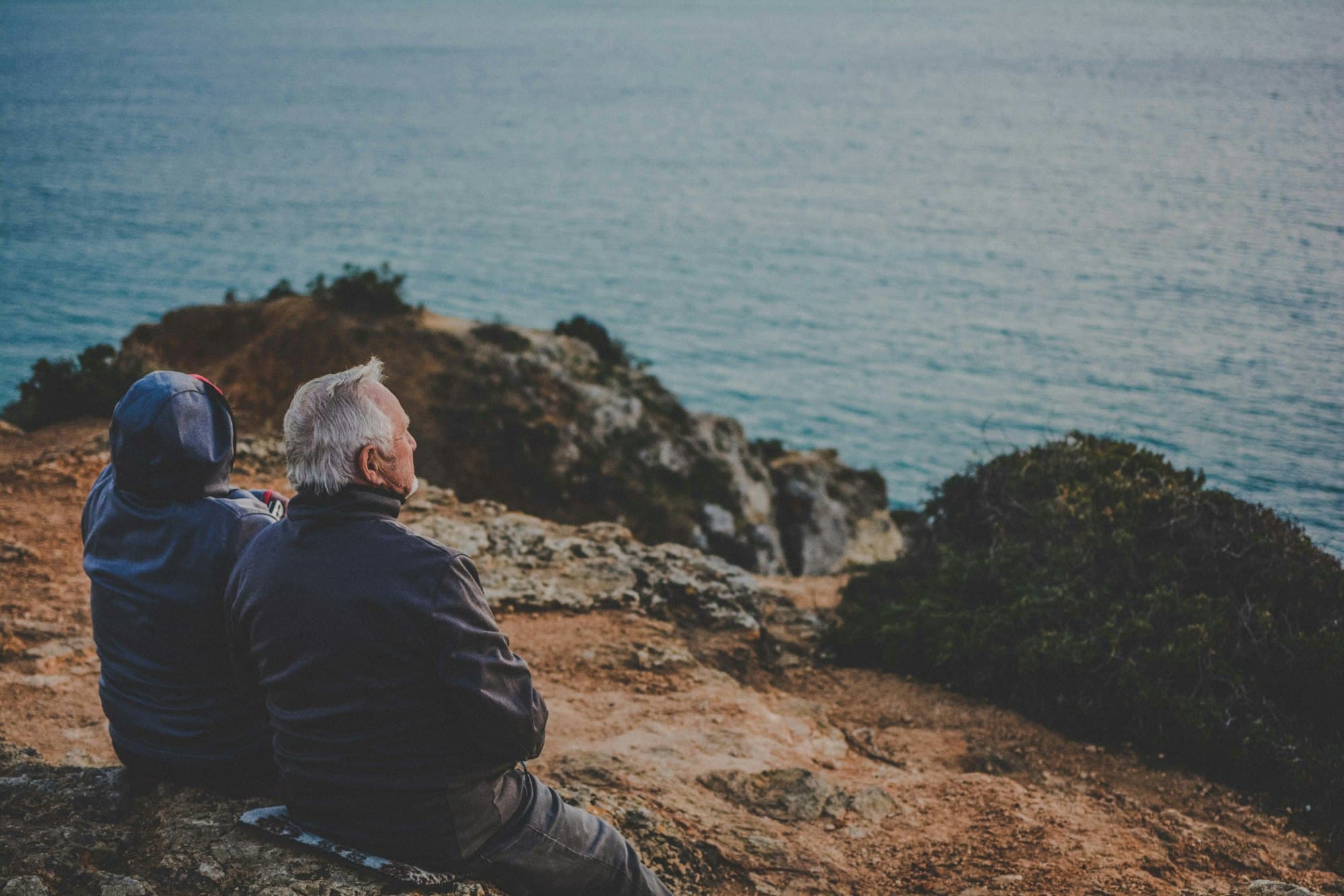 An older couple sitting on a clifftop, looking out over the sea
